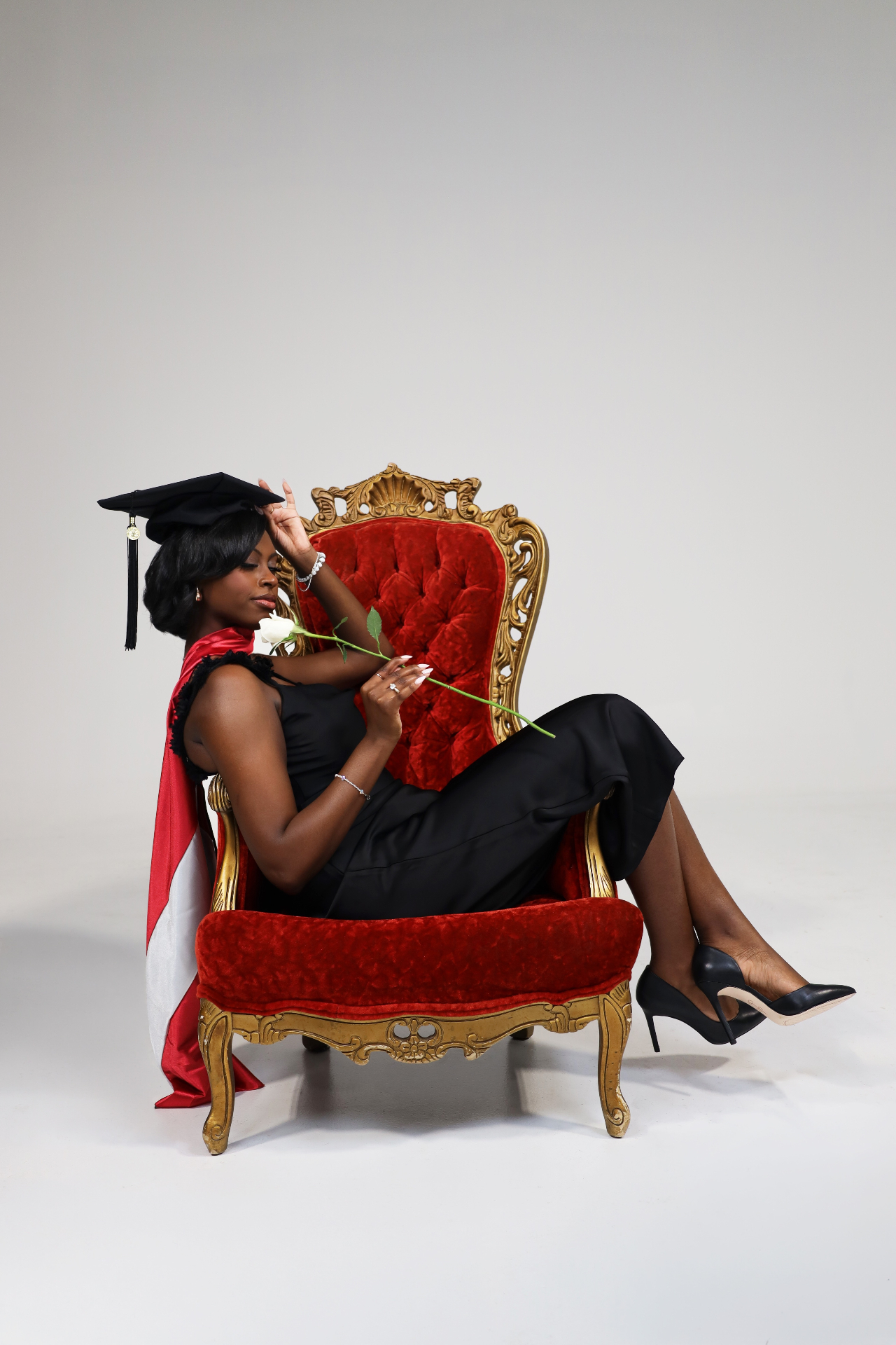 Graduate reclining in an ornate red velvet chair holding a white rose