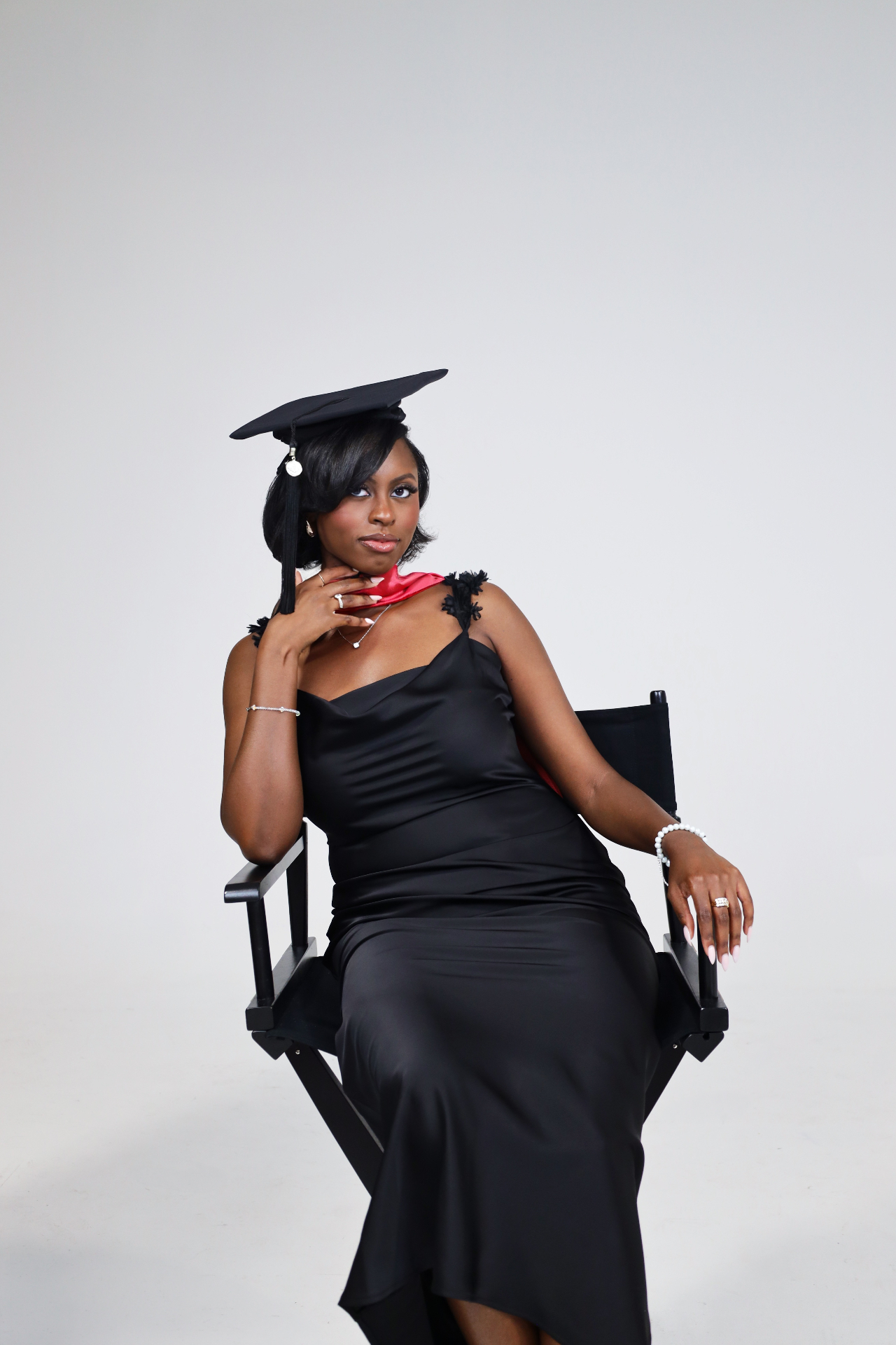 Graduate seated in a director chair wearing a black satin dress and cap