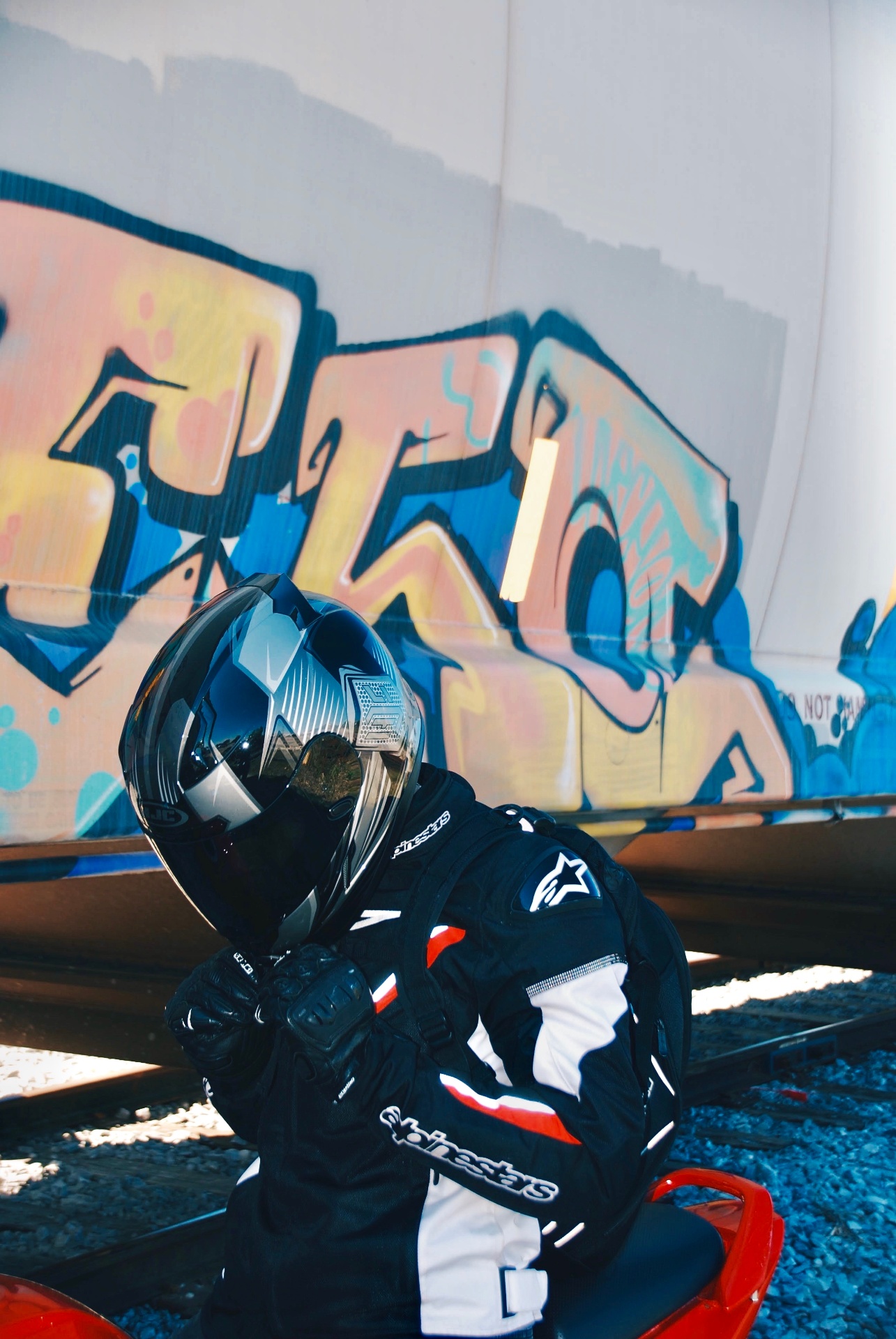 Motorcycle rider seated by graffiti and rails