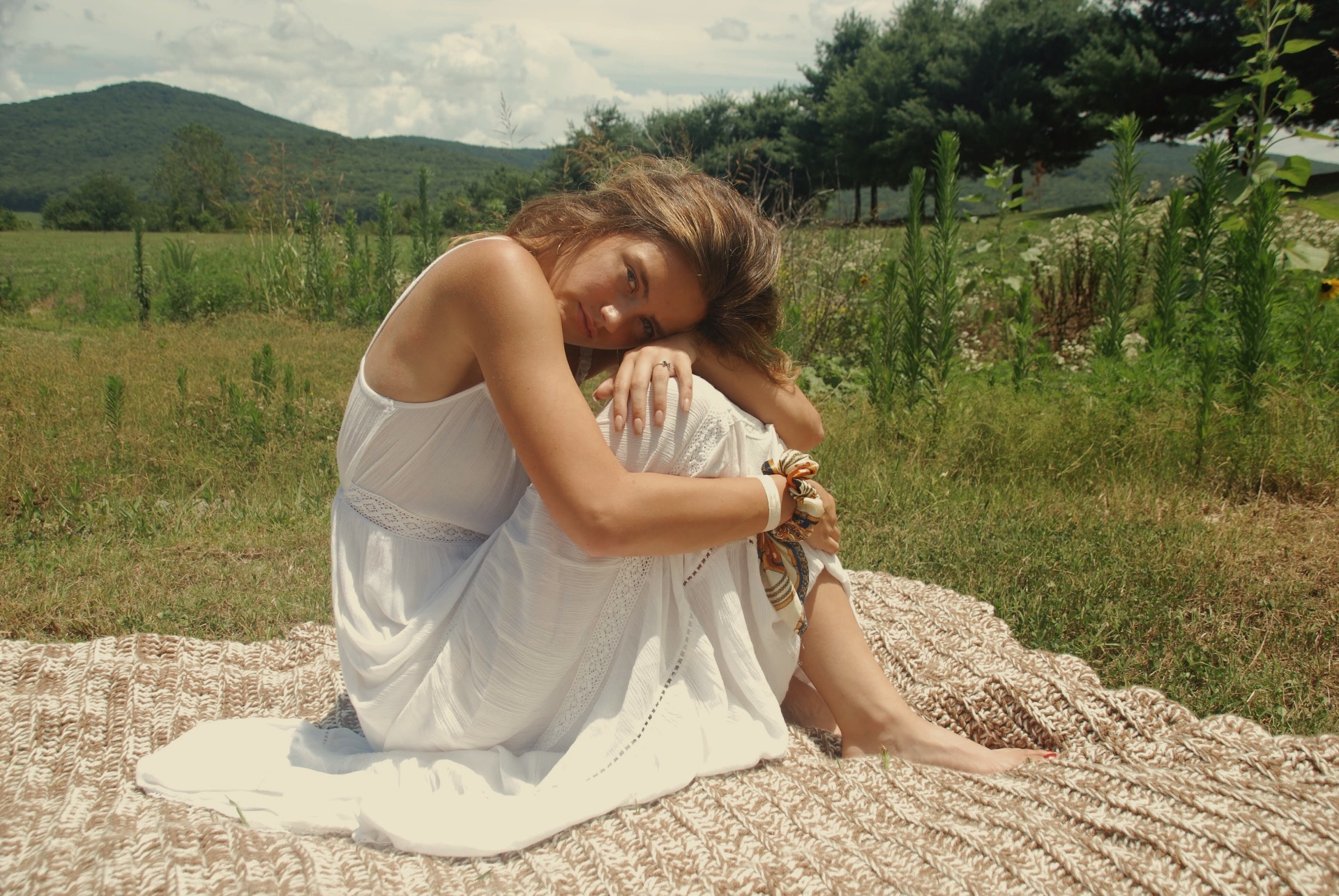 Model seated on a knit blanket in a mountain meadow