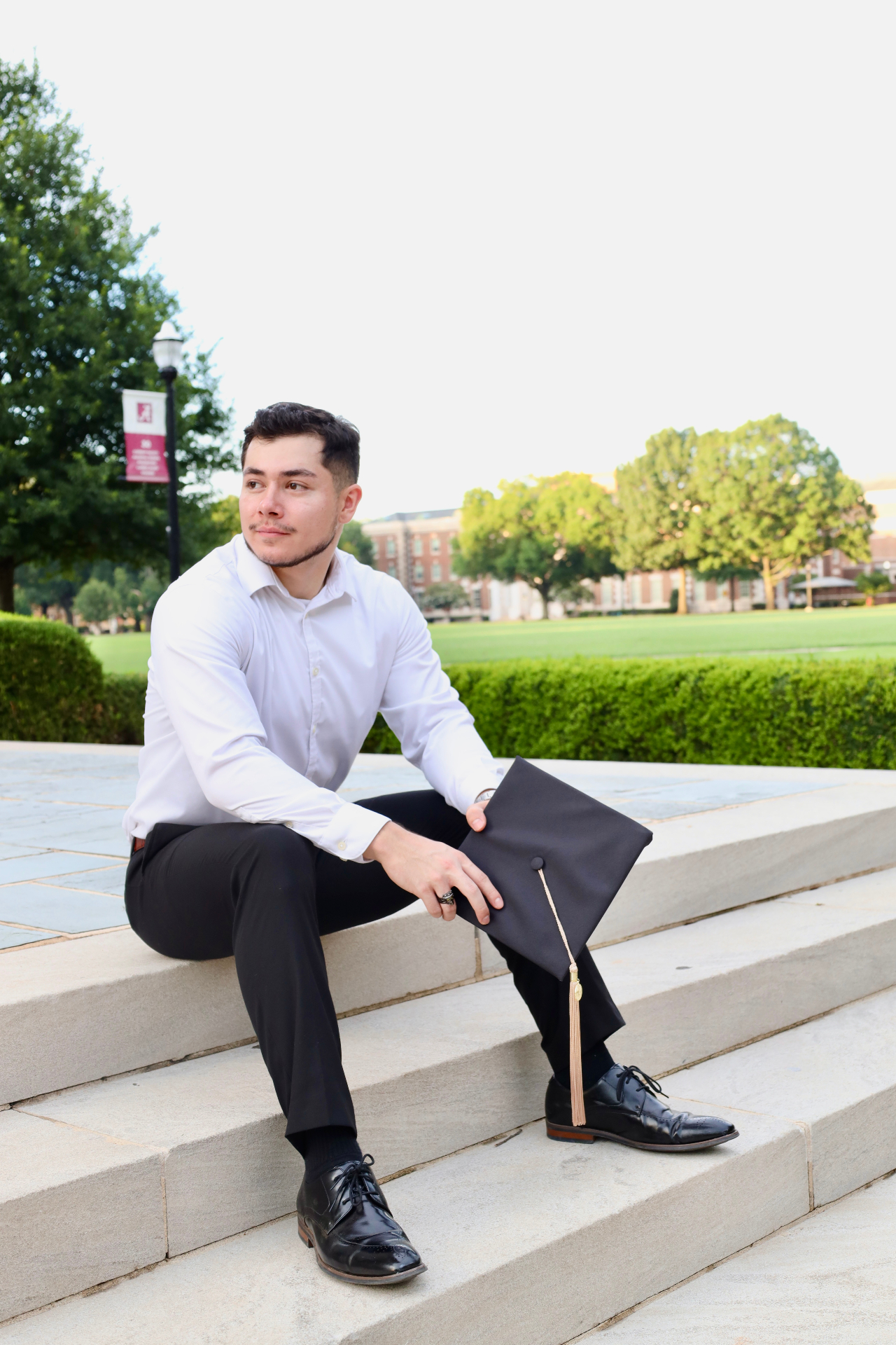 Graduate seated on stone steps holding a black mortarboard