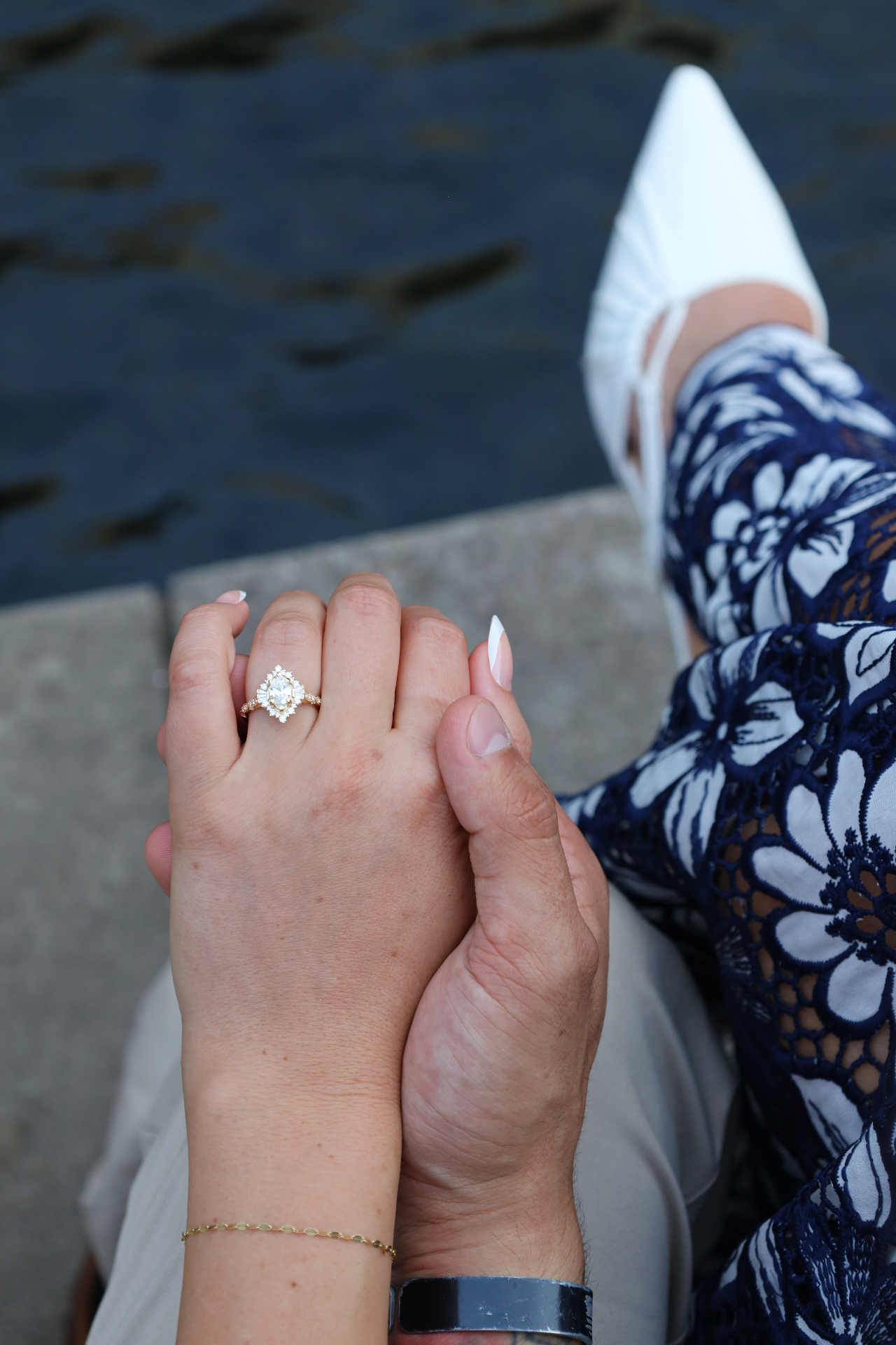 Close-up of engagement ring on clasped hands above the water