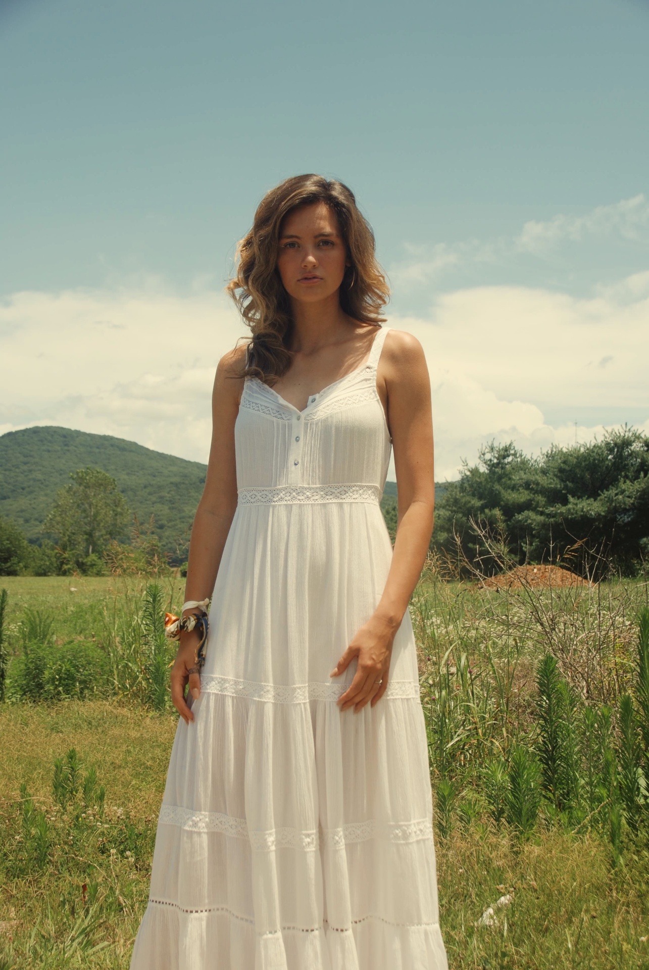 White dress portrait standing in a meadow beneath open sky