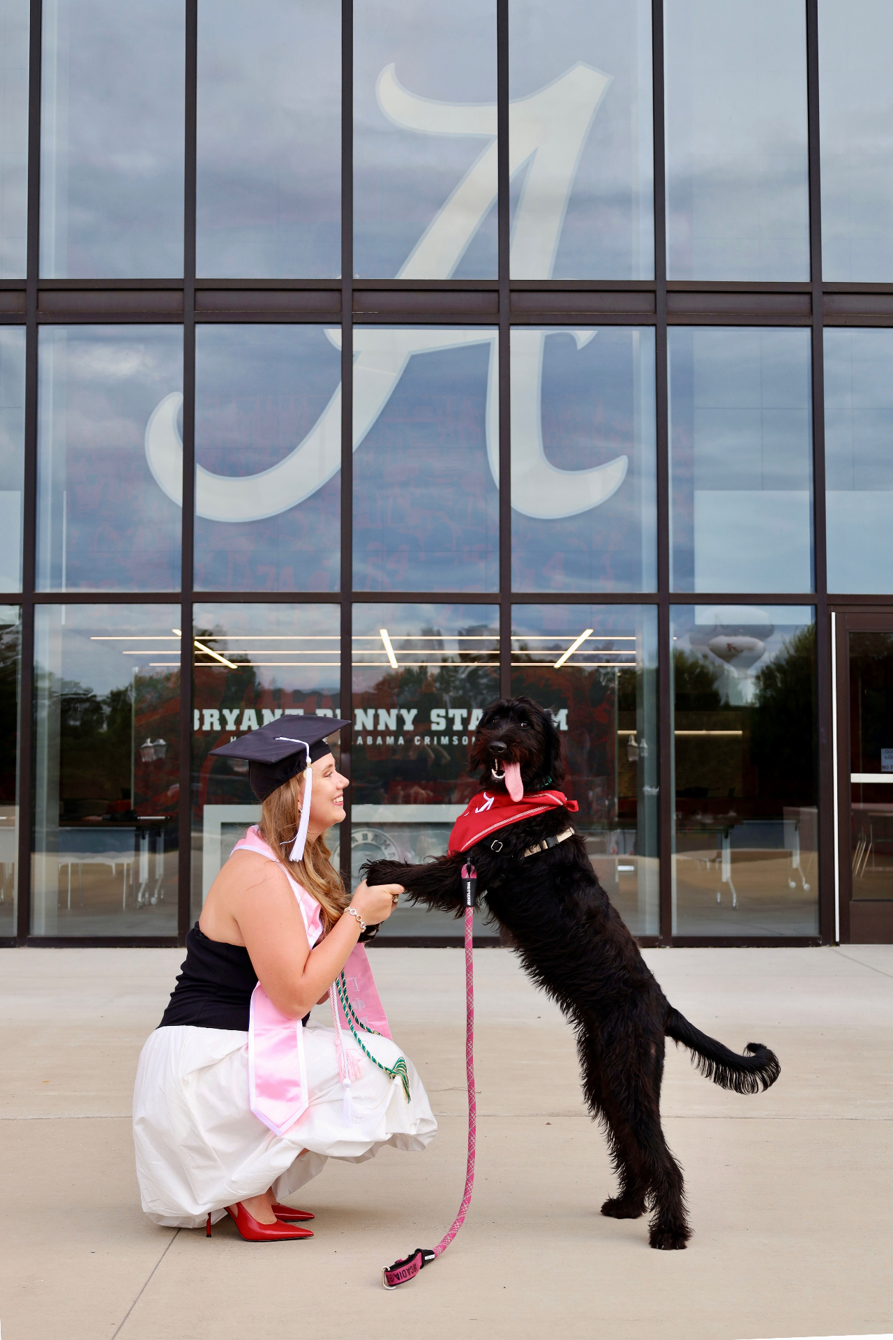 Graduate kneeling with her dog in front of Bryant-Denny Stadium