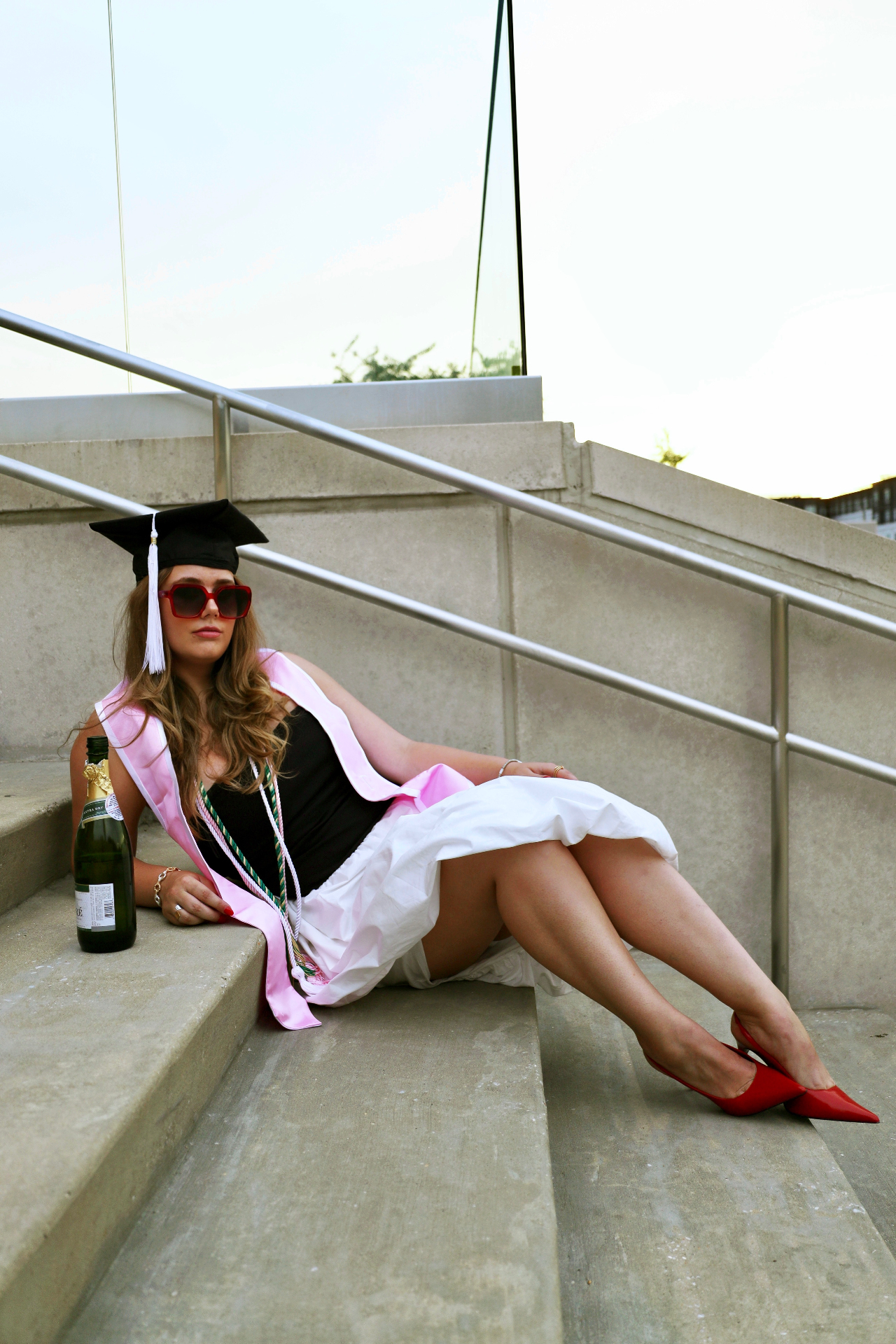 Graduate reclining on concrete steps with champagne and red heels
