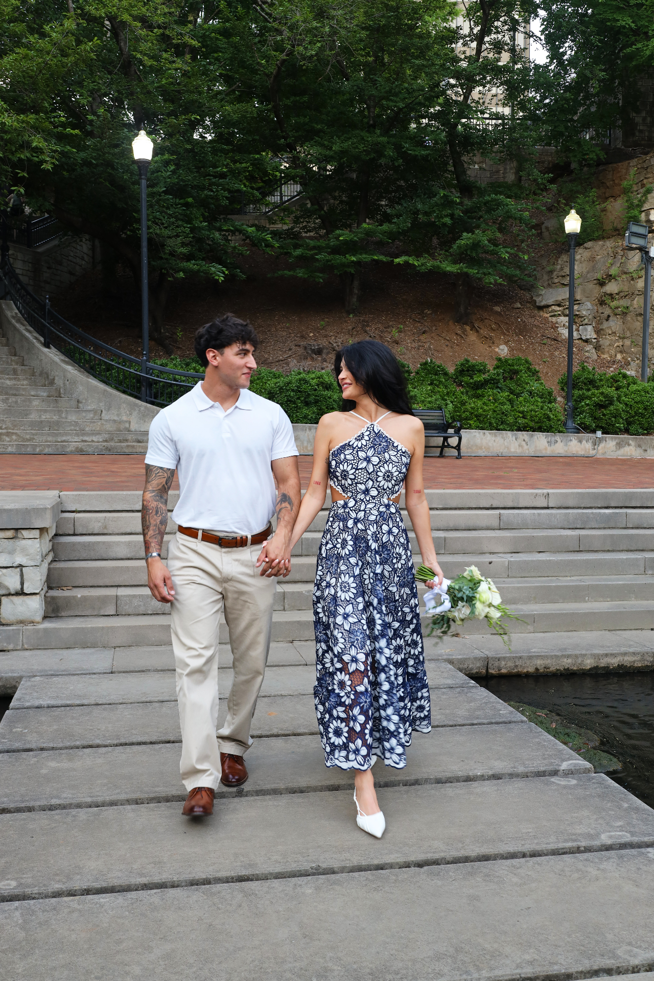 Couple walking hand in hand along a city riverwalk with bouquet