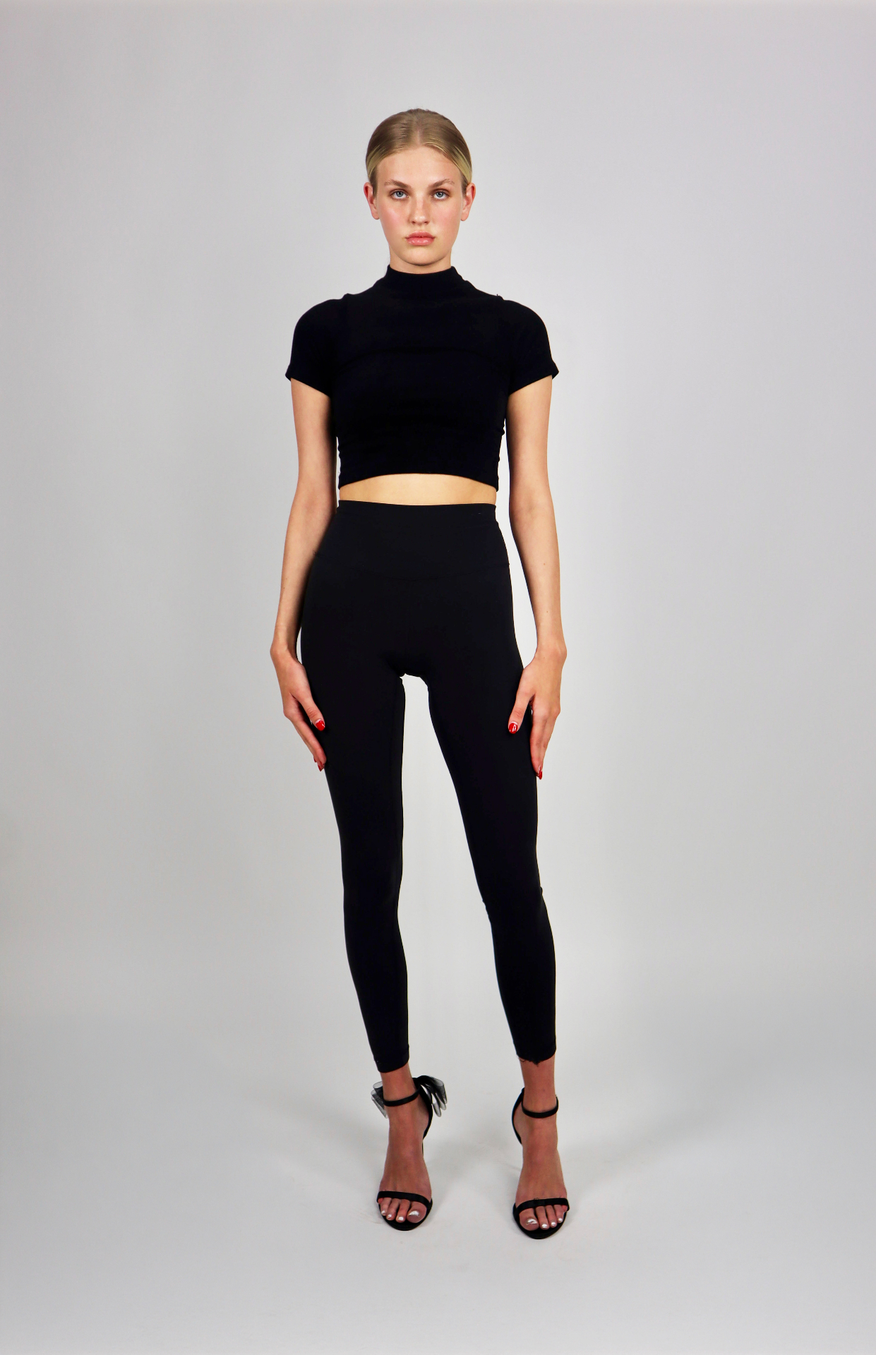 Full-length studio portrait in black mock-neck crop top and leggings
