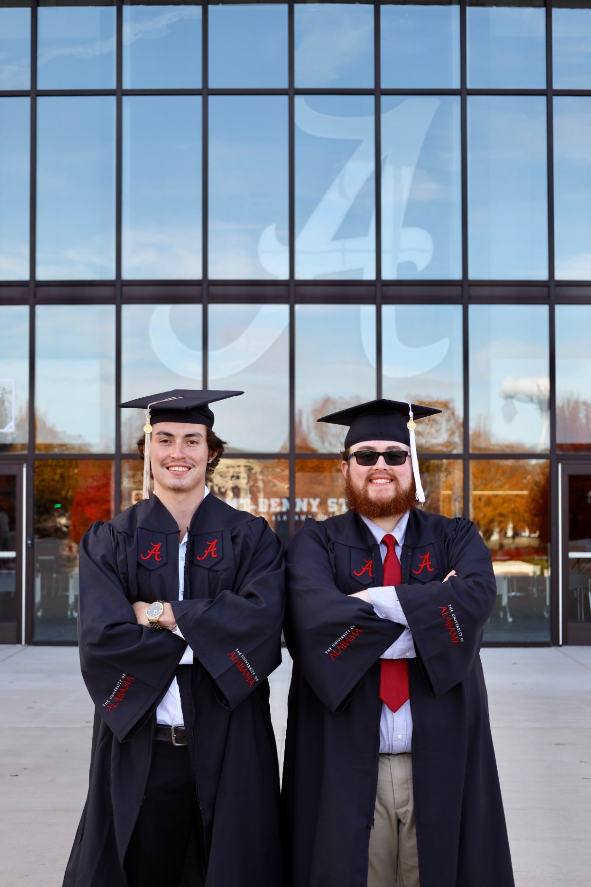 Two graduates posing in cap and gown outside the stadium