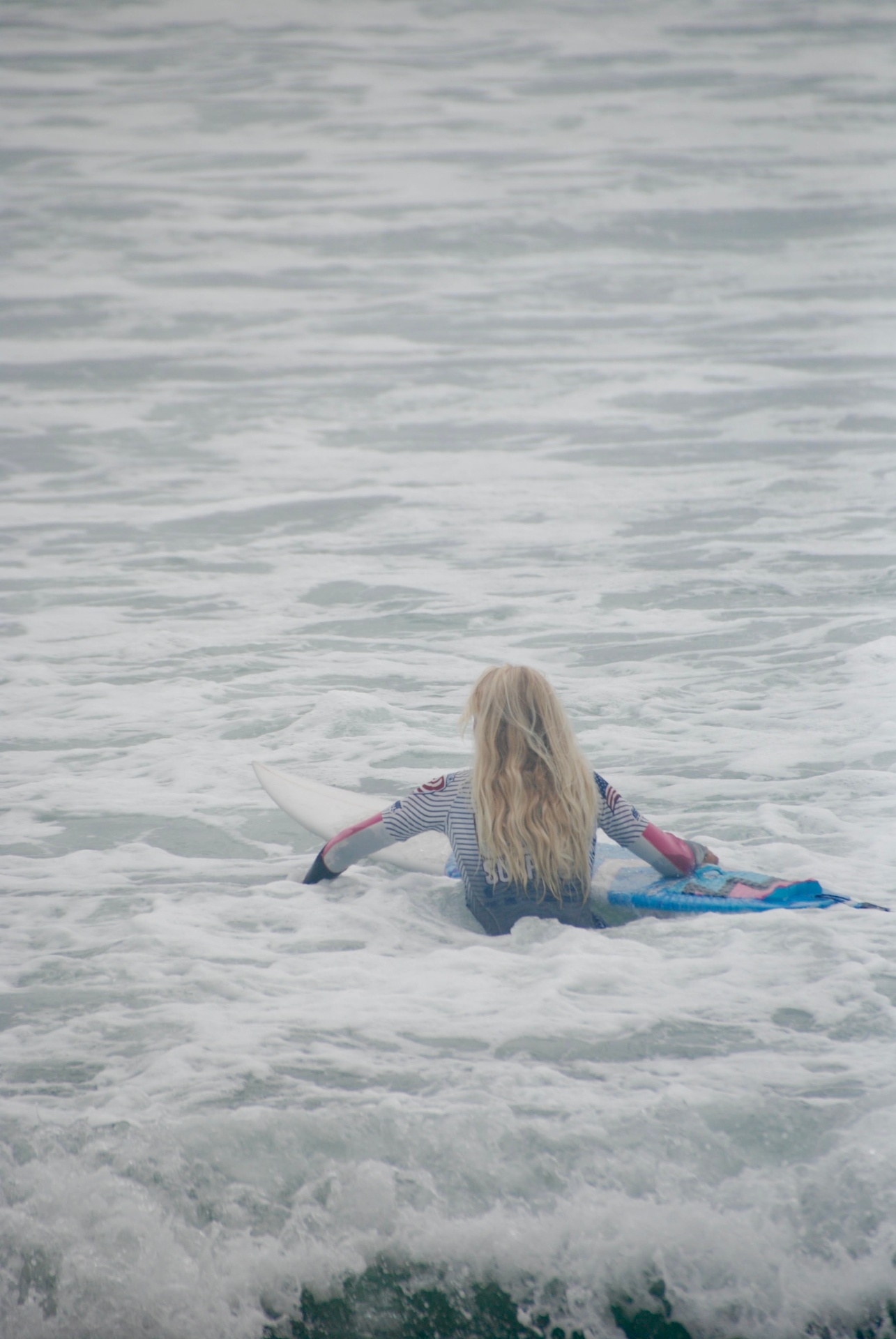 Young surfer paddling out through coastal whitewater